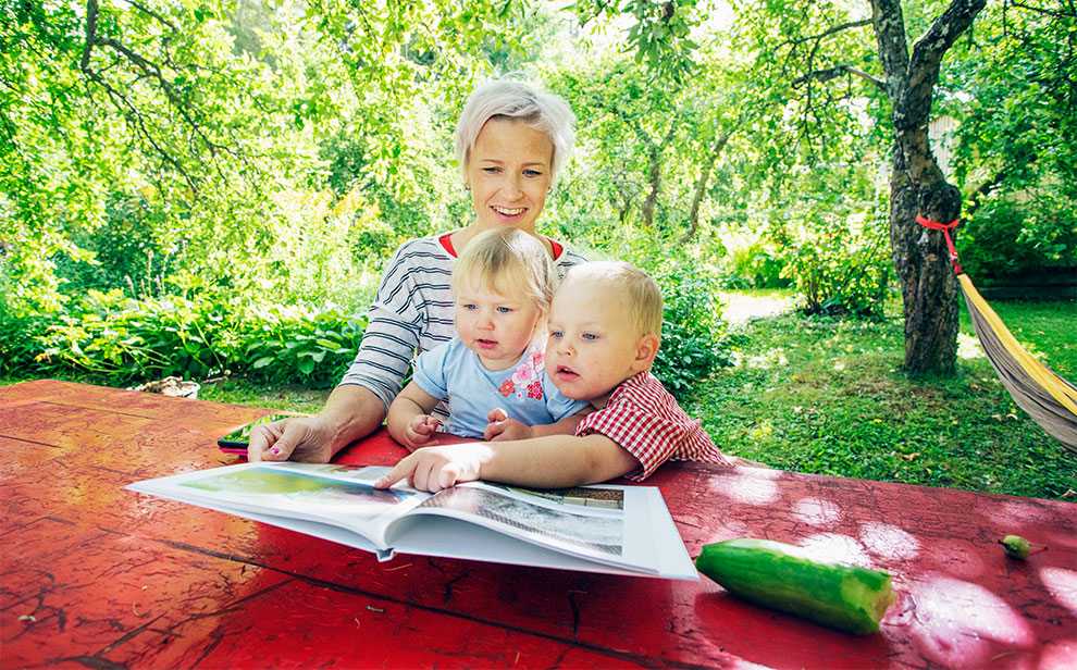 Äiti ja lapset lukevat kuvakirjaa puutarhassa Äiti ja lapset lukevat kuvakirjaa puutarhassa